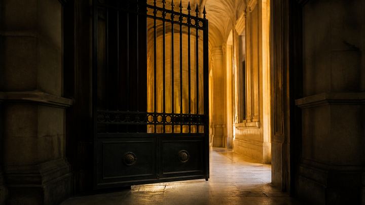 Heavy dark iron gate half closed across a gold-lit stone corridor